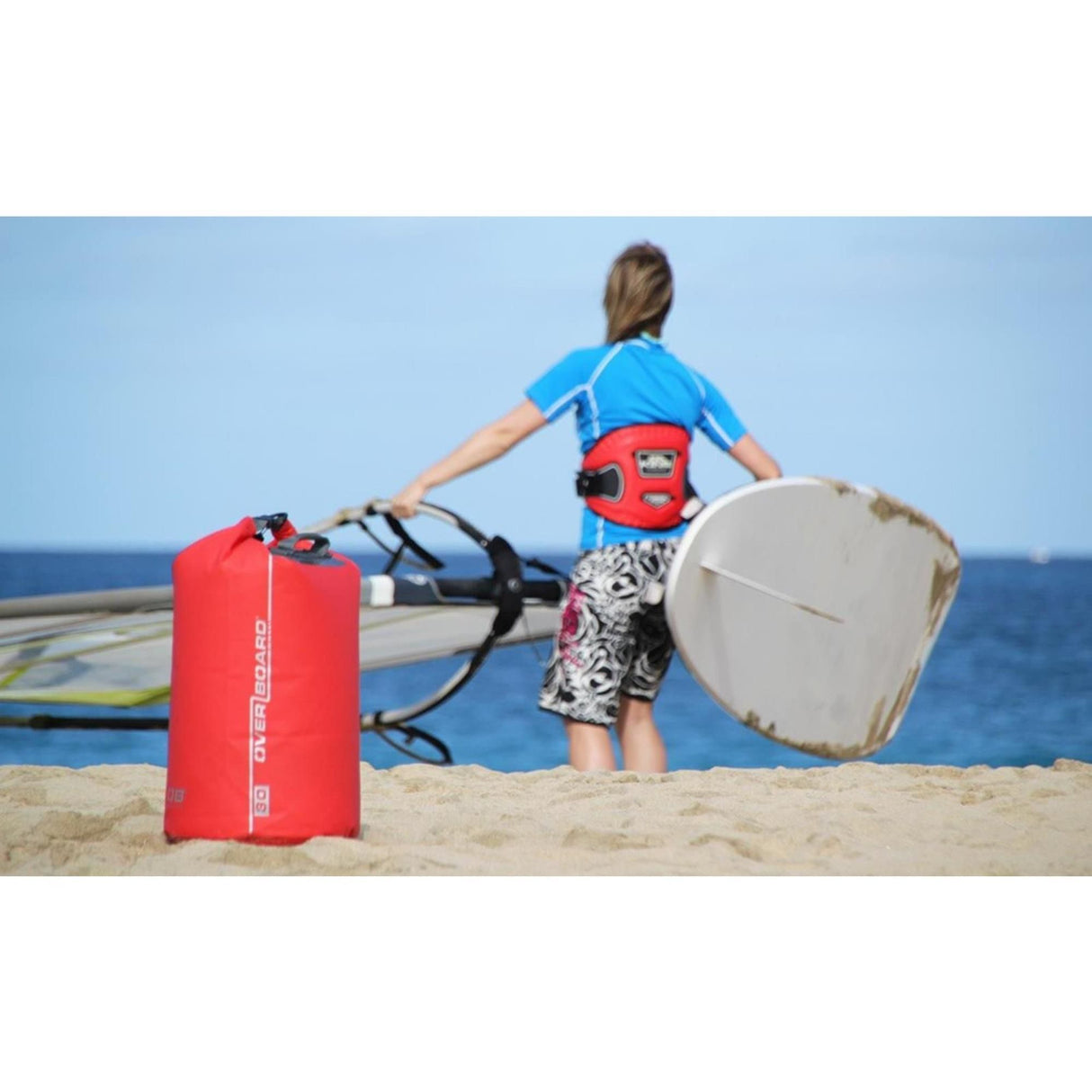 OverBoard wasserdichter Packsack 30 Liter rot, Rollverschluss, am Strand neben Windsurferin