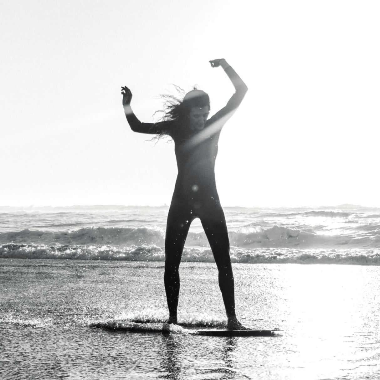 Skimboard SkimOne Palm Beach, weiß-grau, Person im Wetsuit hält Board über Kopf am Strand