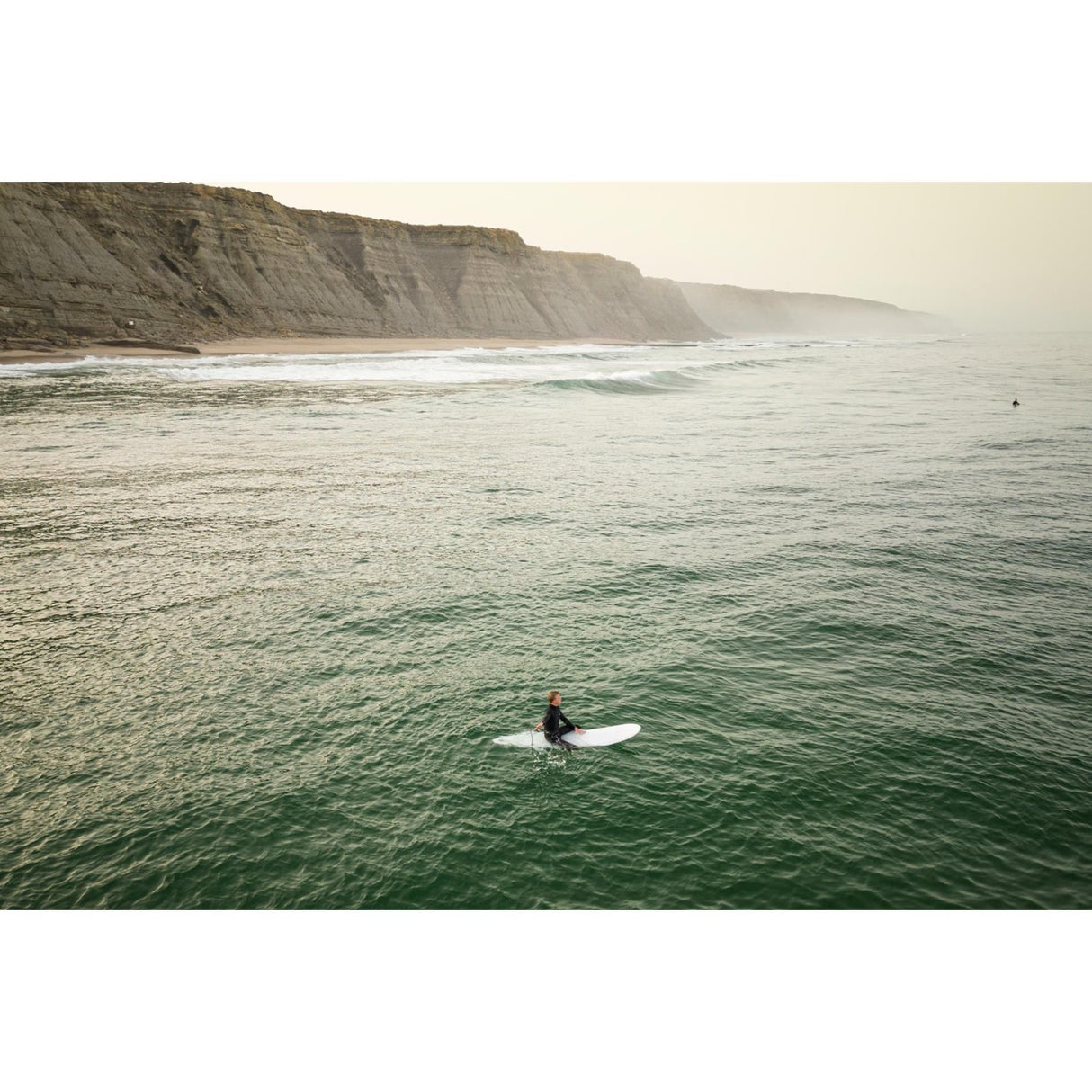 Torq TEC 24/7 Surfboard weiß, Surfer im Meer paddelt auf dem Board, Strandszene mit Klippen
