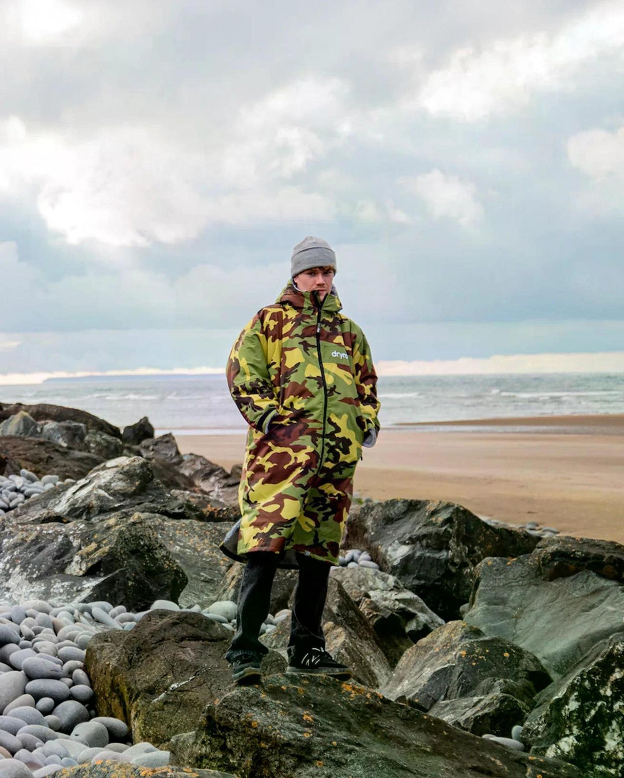 Dryrobe Advance Long Sleeve in Camo-Gelb, getragen am Strand zwischen Steinen, Frontalansicht