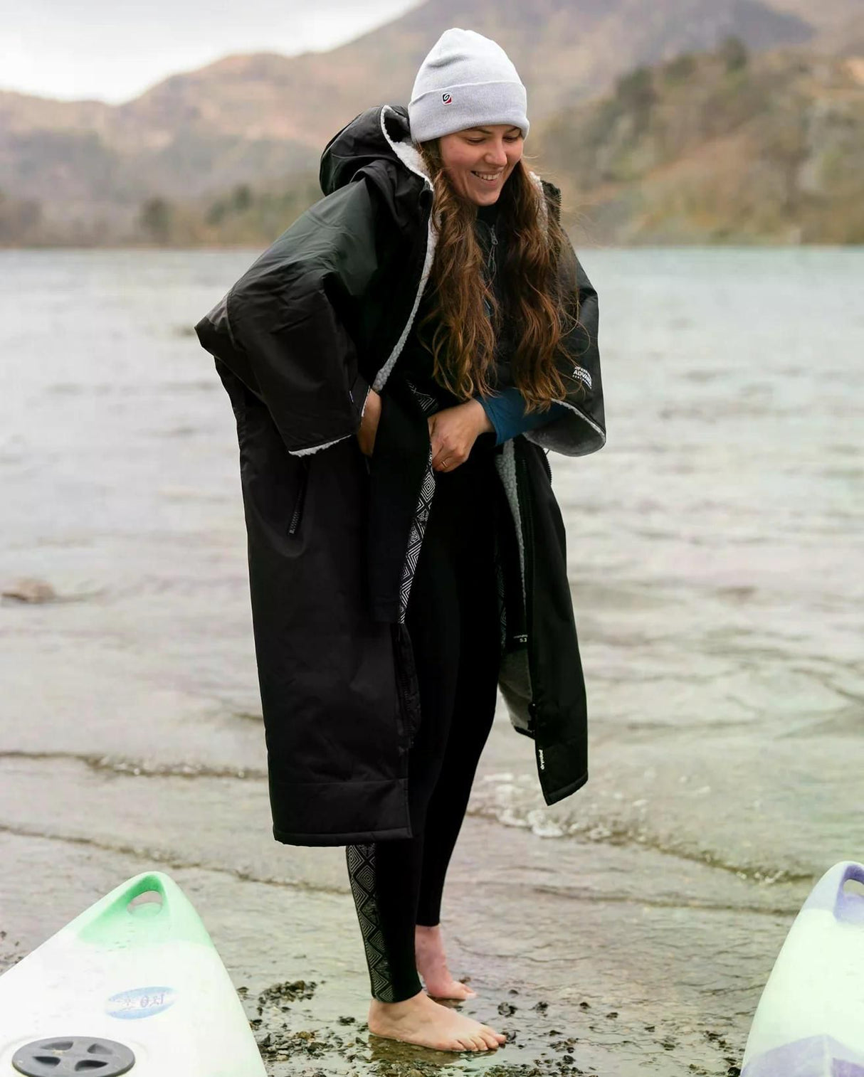 DRYROBE Advance Kurzarm in Schwarz, Frau am Strand mit Surfboards, Funktionsmaterial, Übergangsjacke
