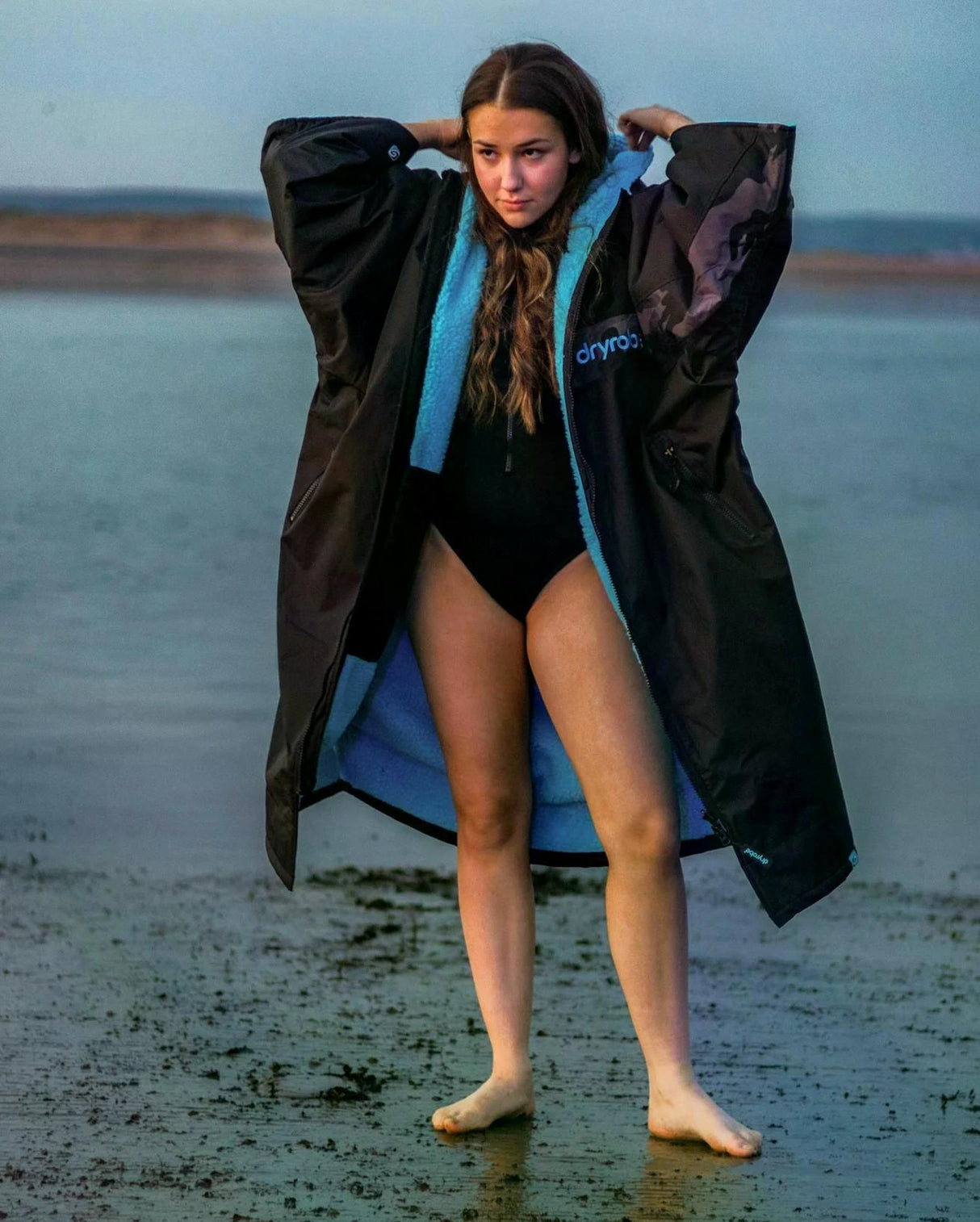 DRYROBE Advance Kurzarm in Schwarz-Blau, Frau trägt Umhang am Strand