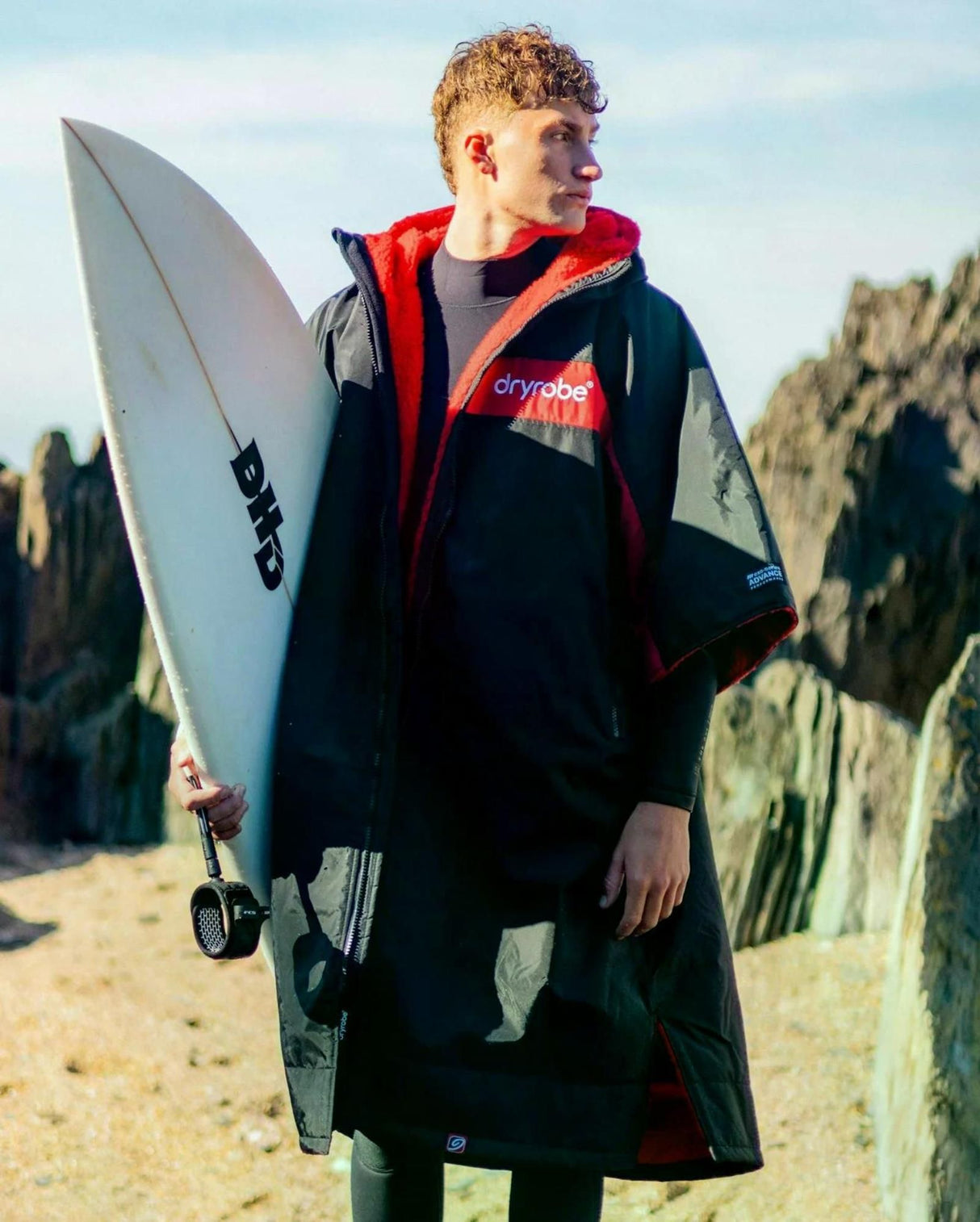DRYROBE Advance Short Sleeve in Rot-Schwarz, Surfer mit Surfboard am Strand, Frontalansicht