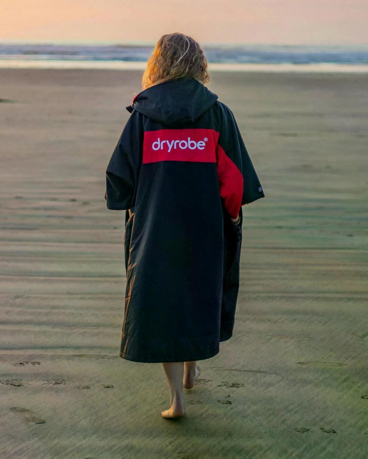 DRYROBE Advance Short Sleeve in Schwarz-Rot, getragen am Strand von hinten, mit Logo-Print