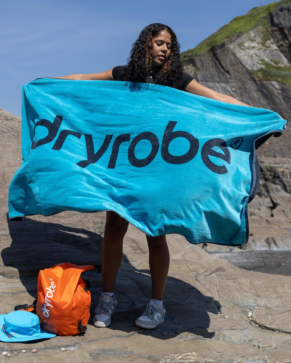Dryrobe Strandtuch in Blau mit schwarzem Logo, Frau am Strand hält Handtuch, schnelltrocknend