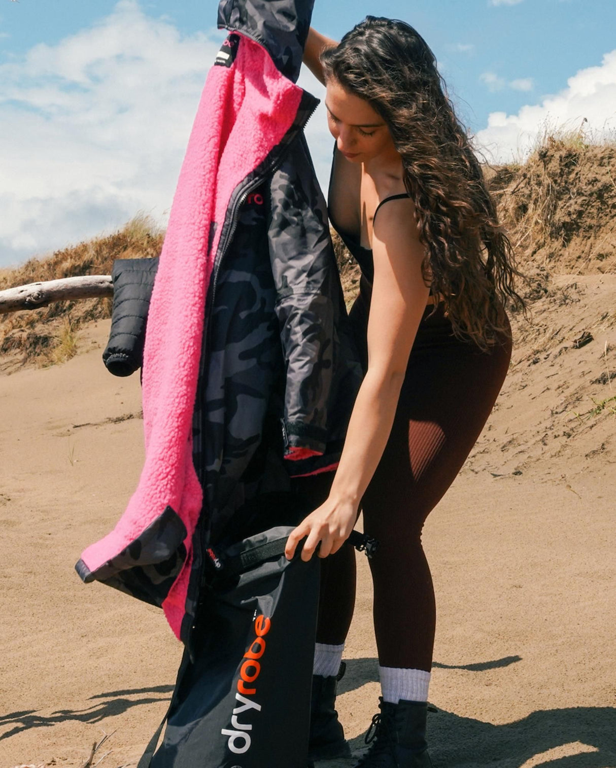 Dryrobe wasserdichter Packsack in Pink und Schwarz, von Person am Strand gehalten, zeigt kompaktes Drybag-Design