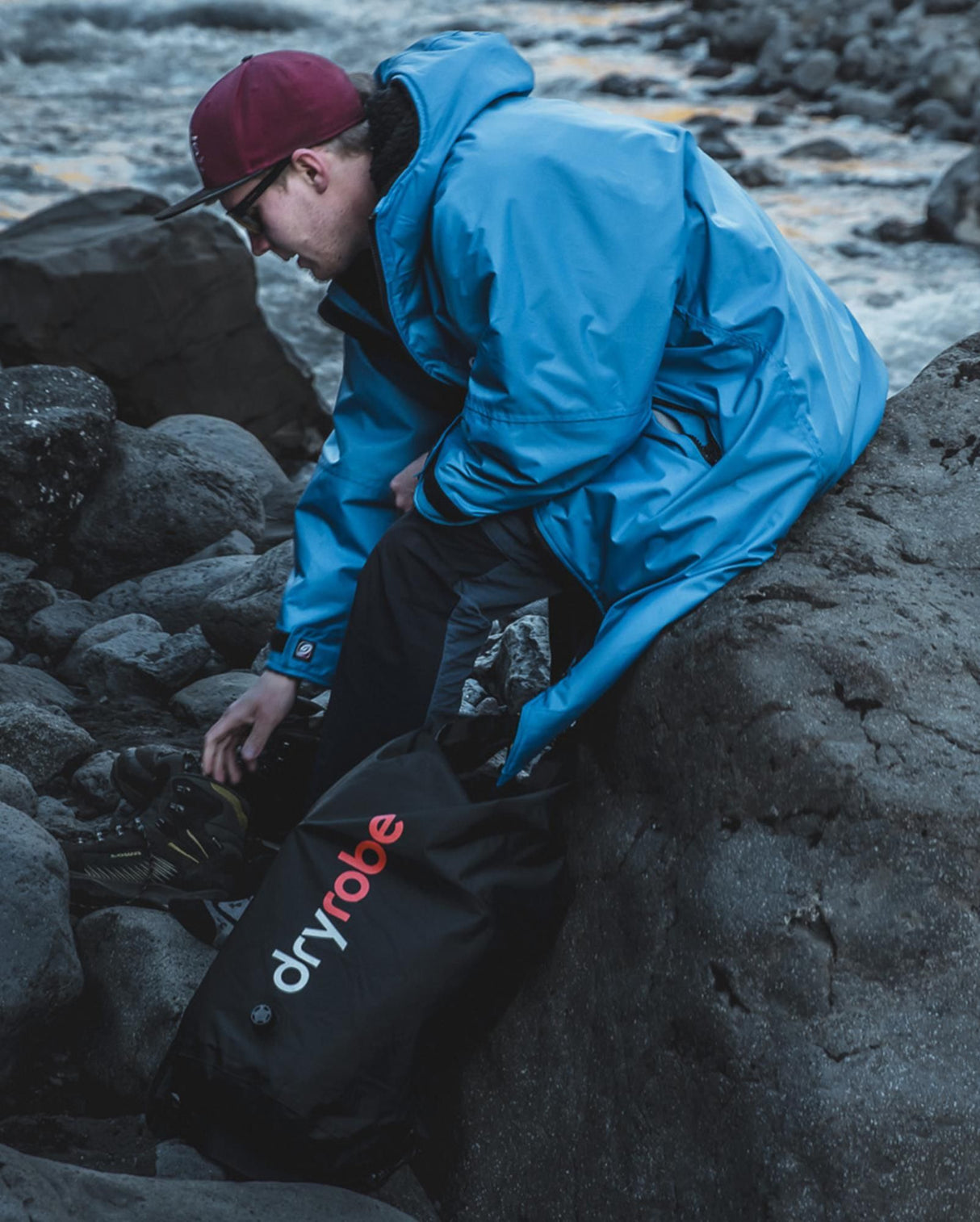 Dryrobe schwarzer wasserdichter Packsack Drybag am Strand, Person in blauer Jacke packt Tasche