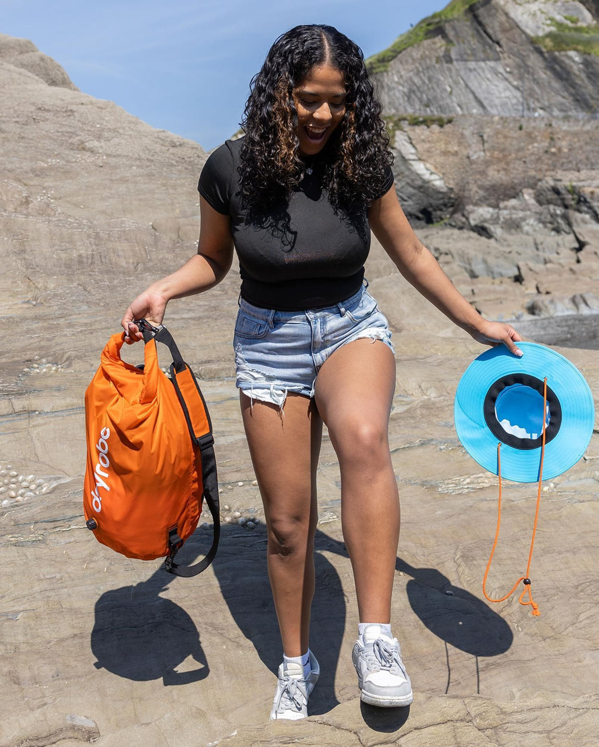 Dryrobe Drybag wasserdichter Packsack in Orange und Blau, von einer Person am Strand gehalten