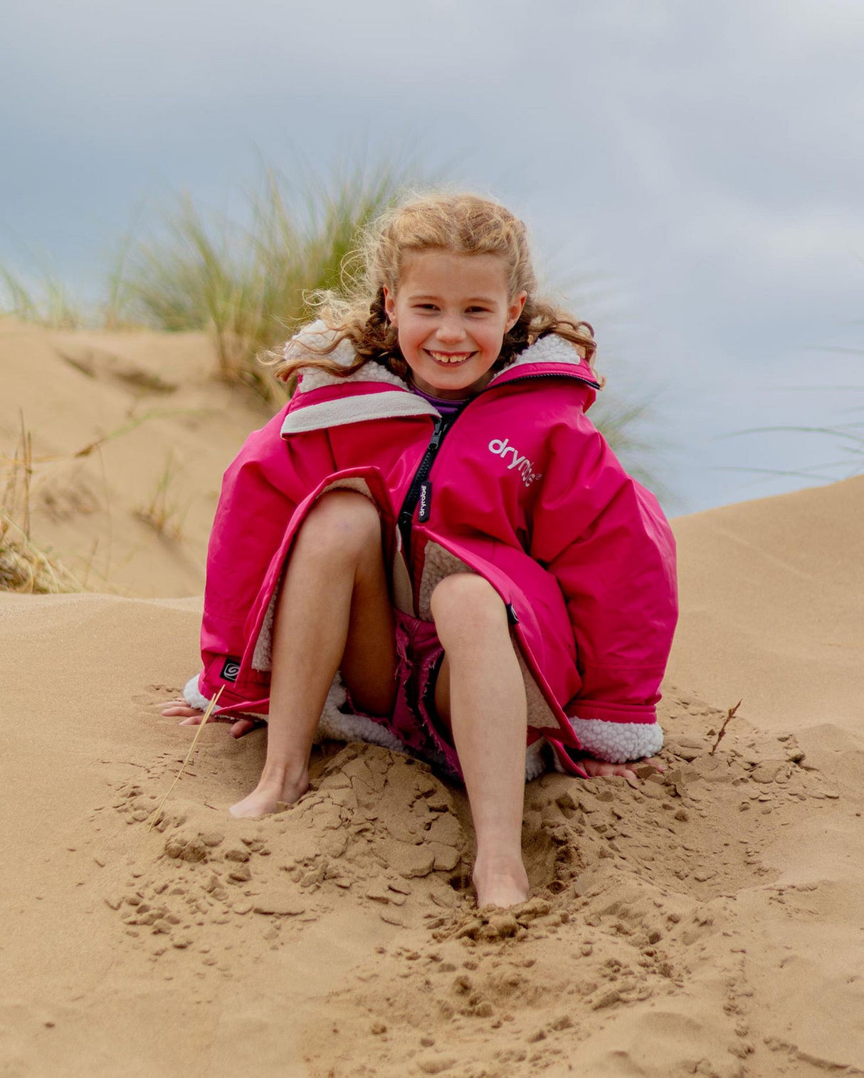 Dryrobe Advance Long Sleeve Kids in Pink mit weißen Streifen, Mädchen sitzt am Strand