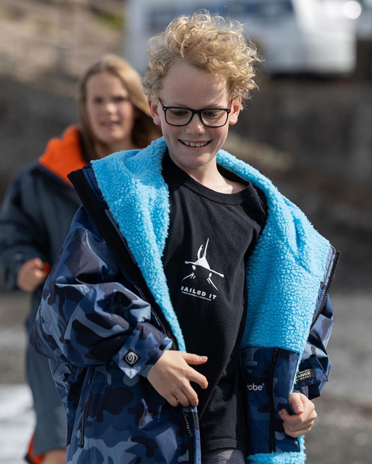Dryrobe Advance Langarm Kinder in Blau und Marineblau, getragen von lachendem Jungen mit offener Jacke und türkisem Fleece-Innenfutter