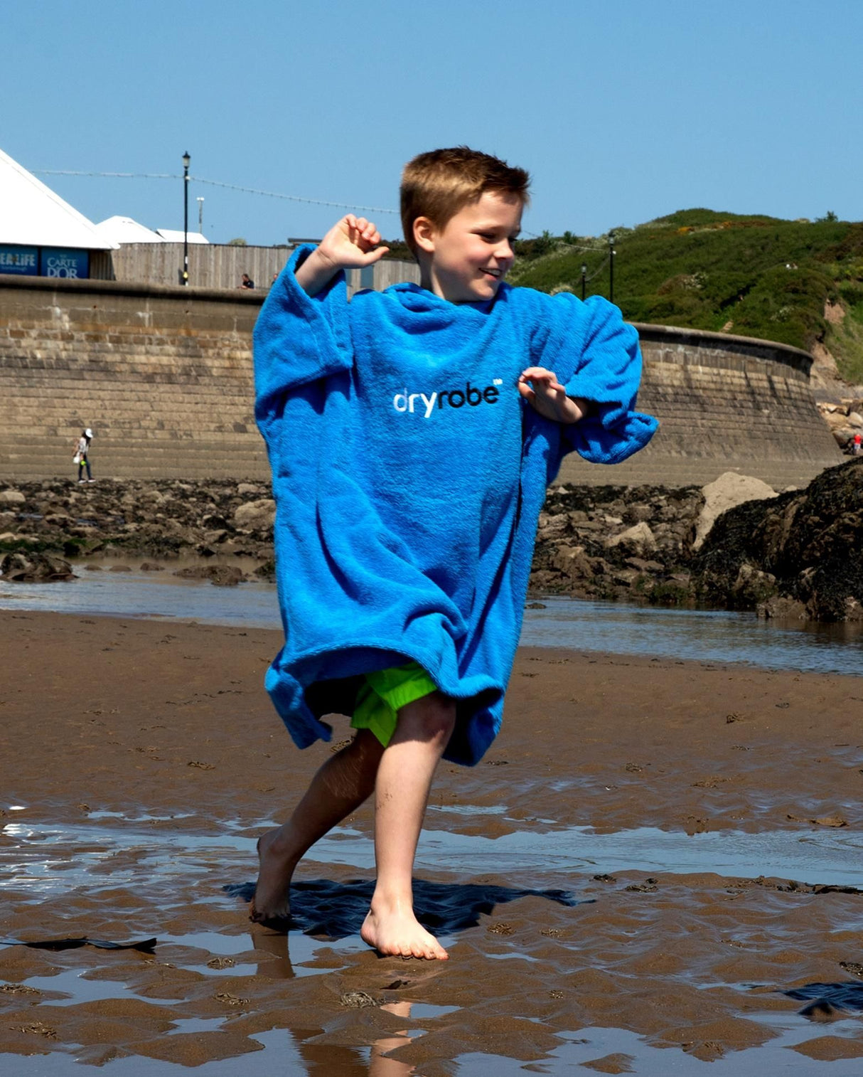 Dryrobe Handtuchmantel Bio Kids in Blau, Kind trägt den Bademantel aus Bio-Baumwolle am Strand