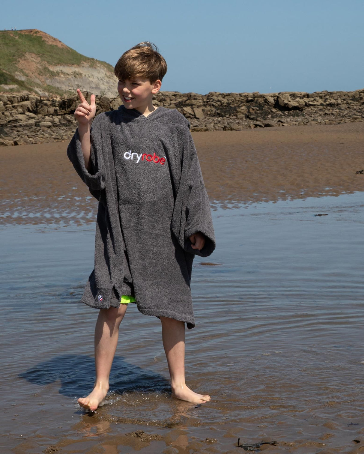 Dryrobe Handtuchmantel Bio Kids in Grau, getragen von Kind am Strand, mit Logo-Print und Kapuze