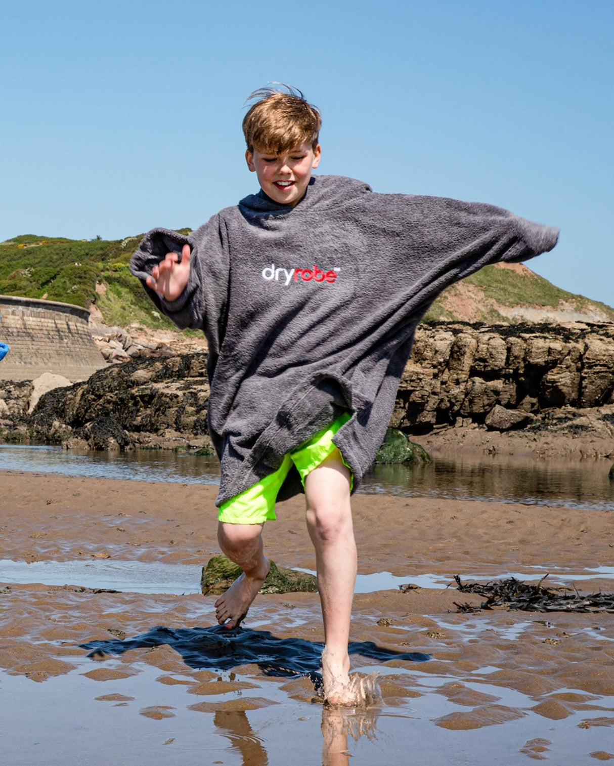 Dryrobe Handtuchmantel Bio Kids in Grau, Kind trägt Umhang am Strand, Bio-Baumwolle, Frontalansicht