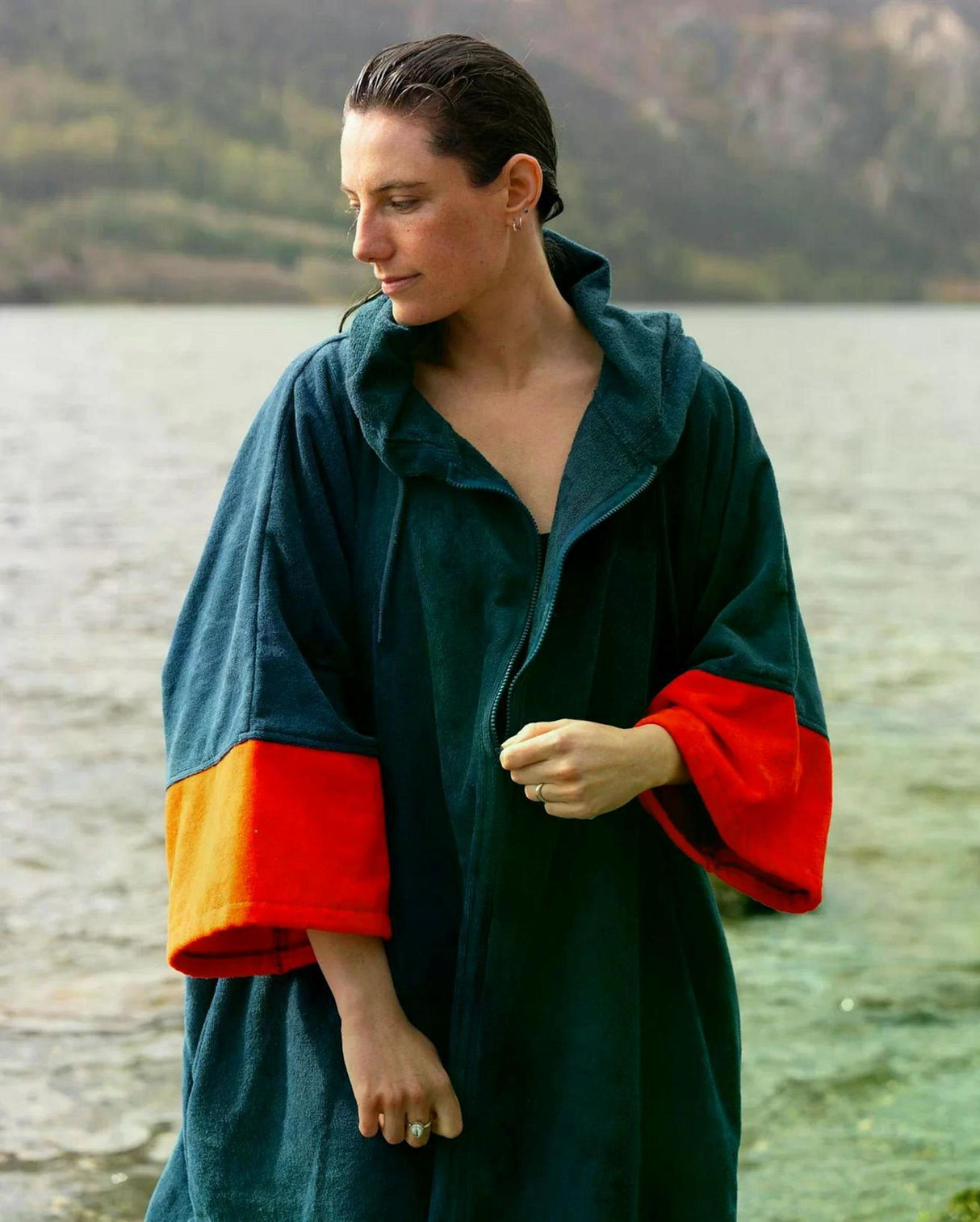 Dryrobe Fullzip Handtuchmantel aus Bio-Baumwolle in Dunkelblau mit roten und gelben Ärmelbündchen, Frontansicht an einem See getragen