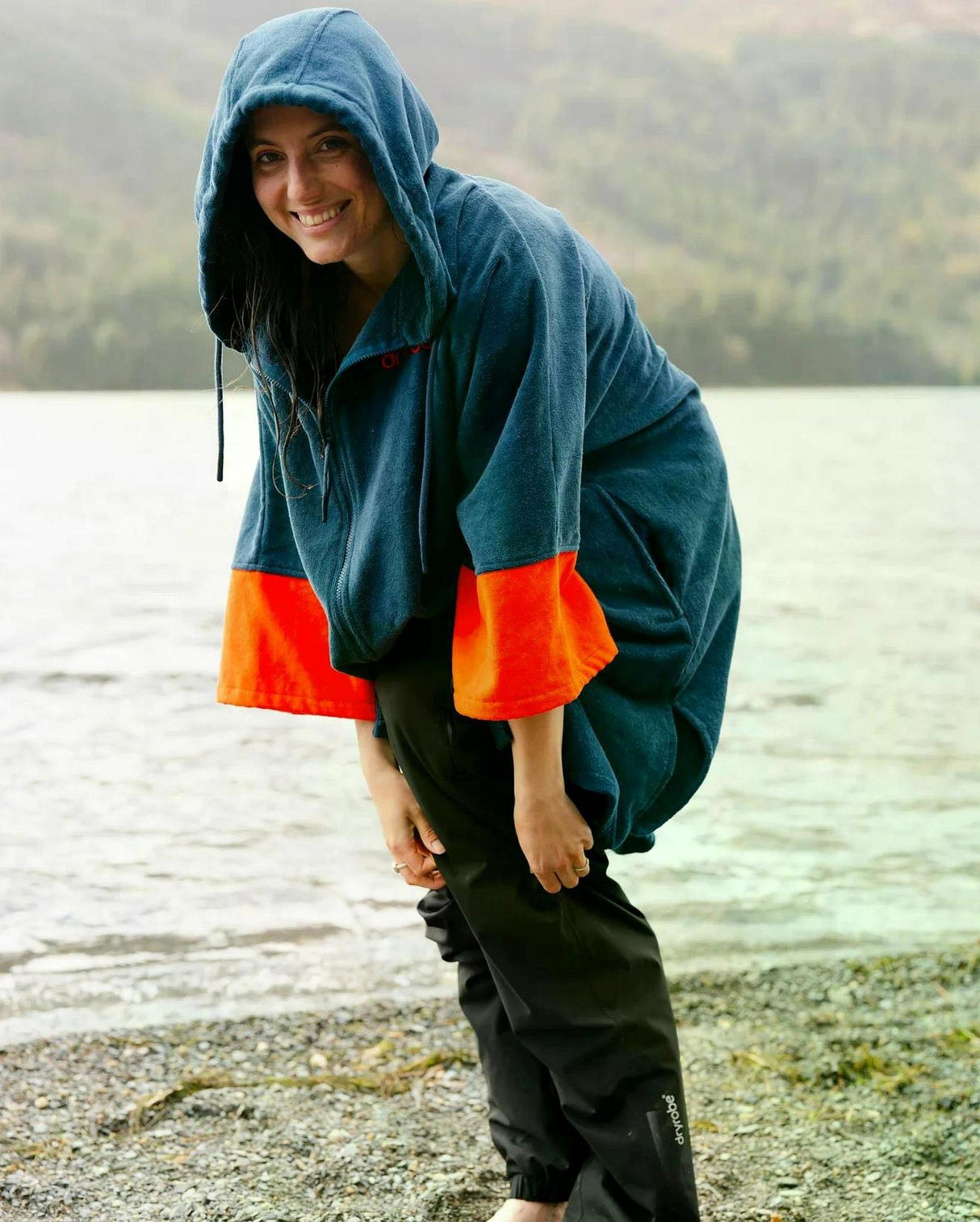 Dryrobe Fullzip Handtuchmantel aus Bio-Baumwolle in Blau mit orangefarbenen Ärmeln, getragen am See
