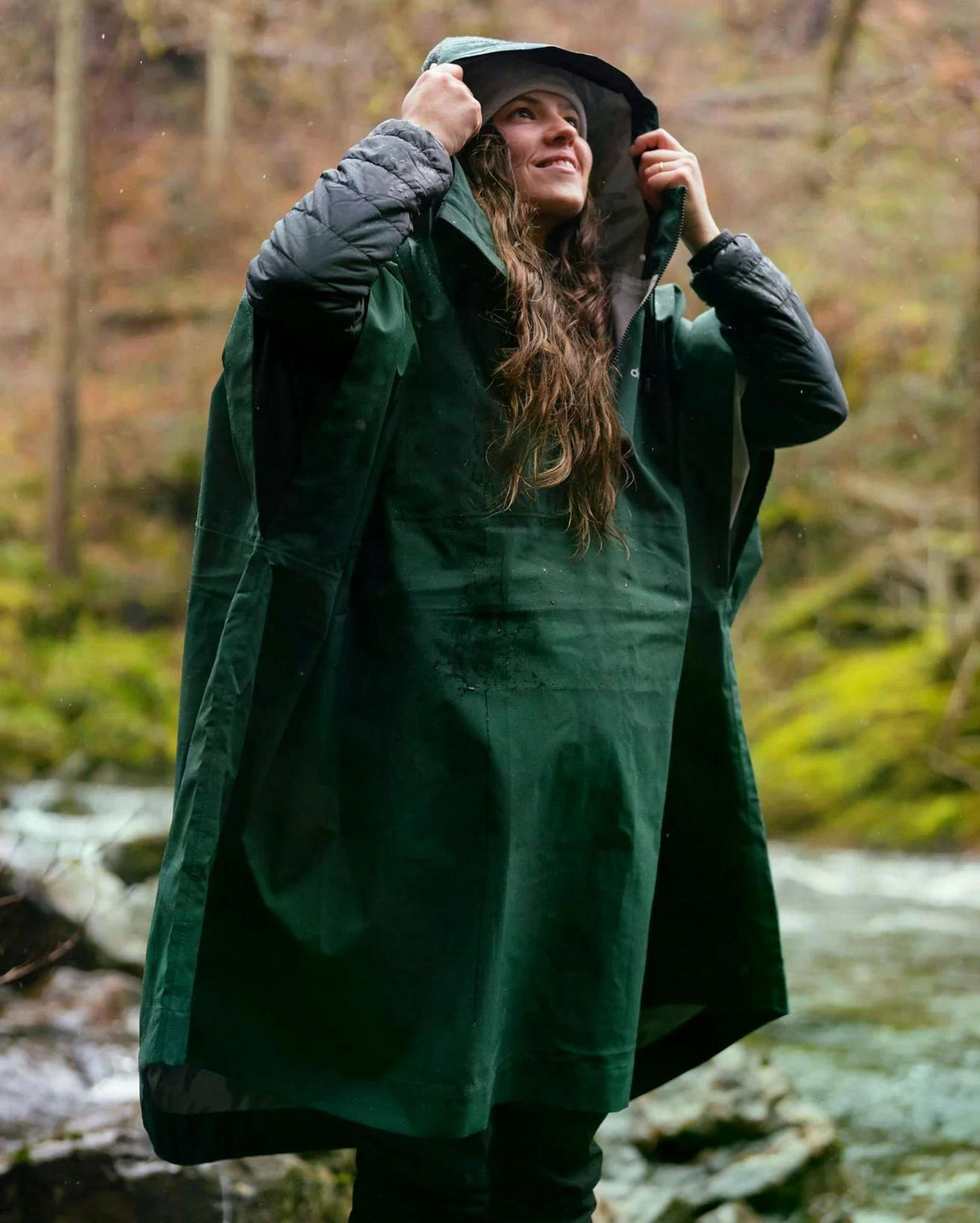 Dryrobe Regen-Poncho in Dunkelgrün, wasserdicht, mit Kapuze, modelliert von Frau in Waldumgebung