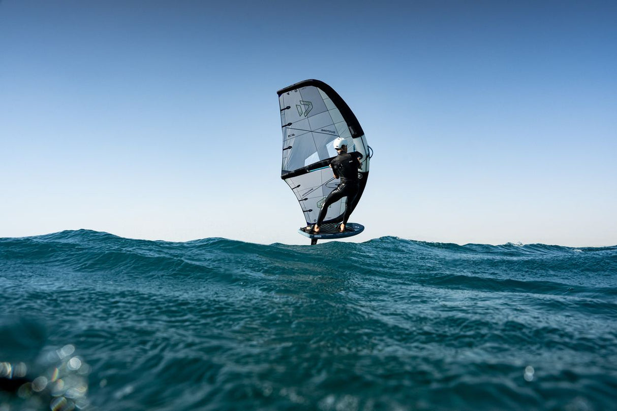Duotone Unit 2027 Kiteboard mit weißem und schwarzem Segel auf türkisem Wasser, Frontansicht, dynamisch positioniert