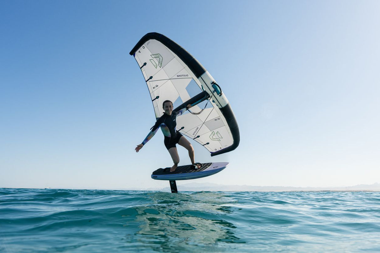 Duotone Unit 2027 Kiteboard mit weißem Segel und schwarzem Rahmen, Fahrer in Aktion über dem Wasser
