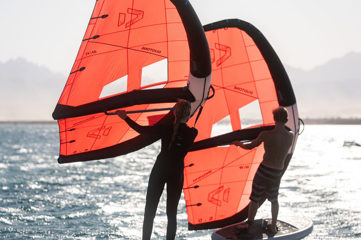 Duotone Unit 2027 Kite rot-orange mit weißen Feldern, schwarze Streben, Frontalansicht am Wasser
