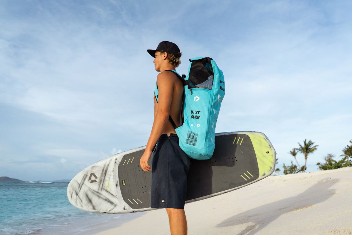 Duotone Unit D/LAB 2027 Kiteboardrucksack in Türkis und Grau, getragen am Strand mit Kite, Frontalansicht