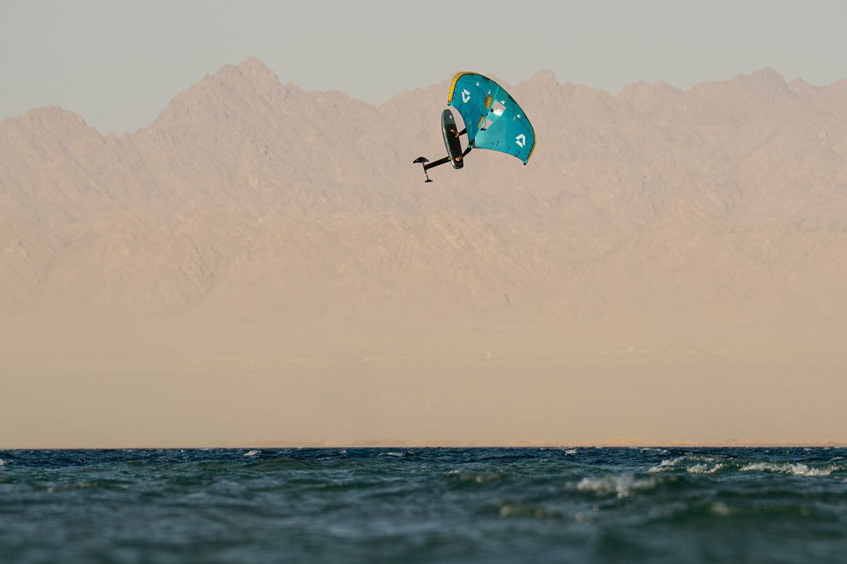 Duotone Unit D/LAB 2027 Kitesegel in Türkis über Wasser vor Wüstenbergen, Seitenansicht