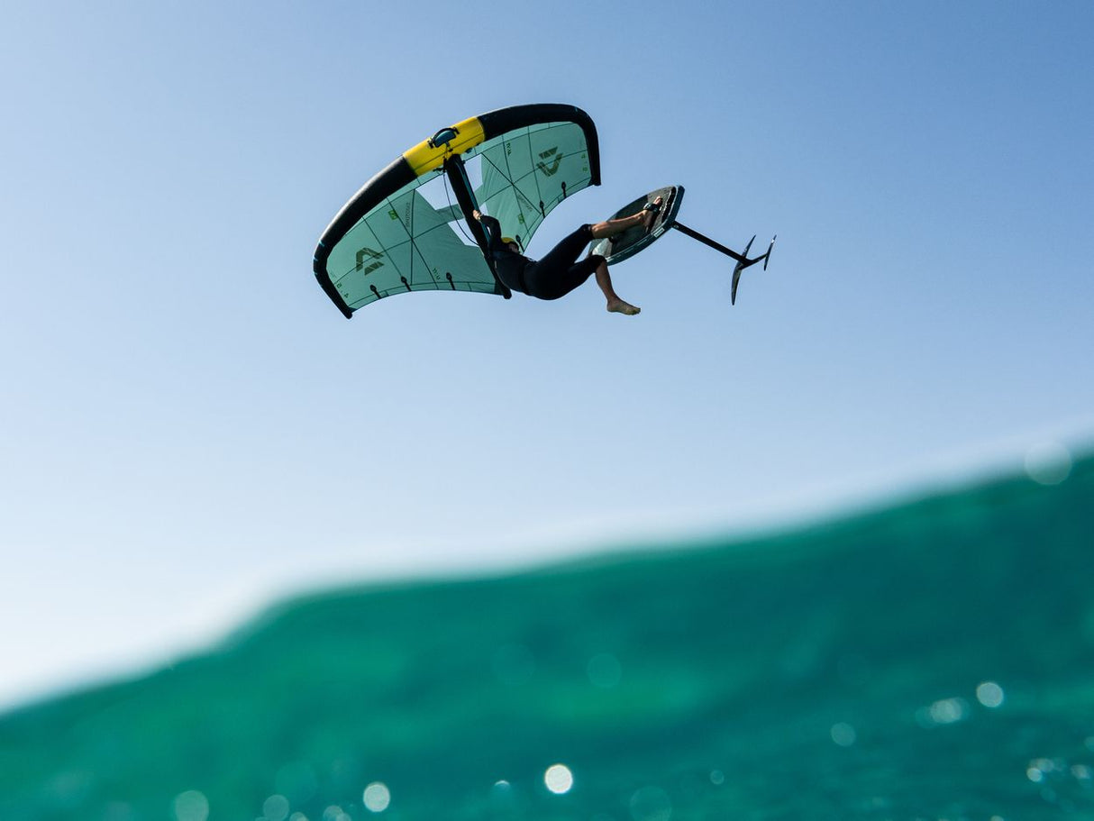 Duotone Unit SLS 2027 Kiteboard in Grün-Gelb-Schwarz, Athlet beim Sprung über Welle, Frontalansicht
