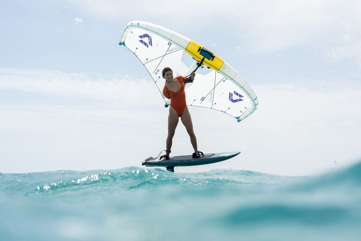 Duotone Unit SLS 2027 Kiteboard mit weißem Segel und gelben Streben, Sportler beim Kitesurfen auf türkisblauem Wasser in Aktion