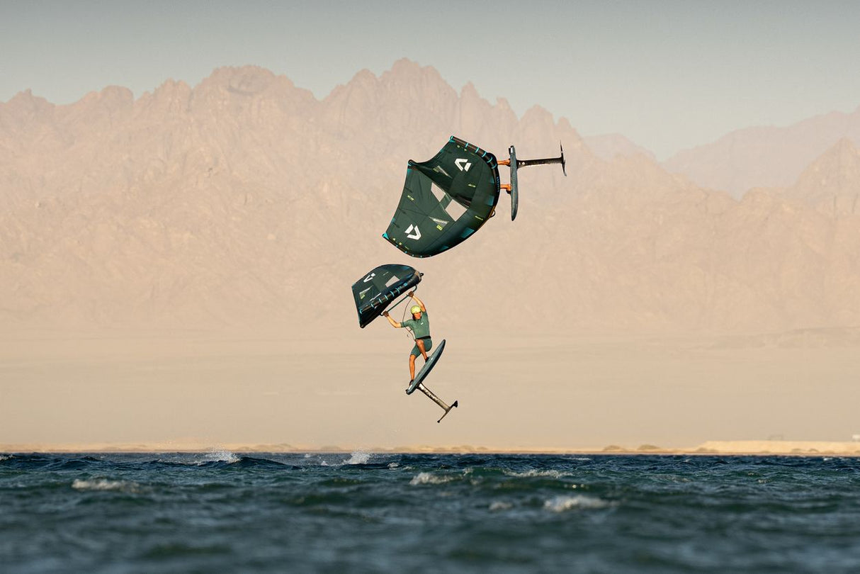 Duotone Sky Style SLS 2027 Kiteboard in Dunkelgrün und Beige, Sprung über Wasser mit Bergkulisse, Seitenansicht