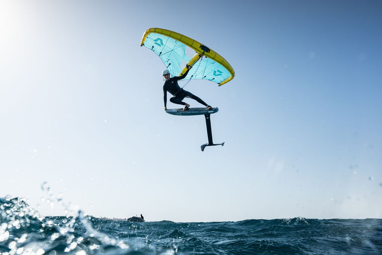 Duotone Sky Style SLS 2027 Kiteboard mit gelbgrünem und blauem Doppelton-Design, Athlet in Aktion über Wasser springend