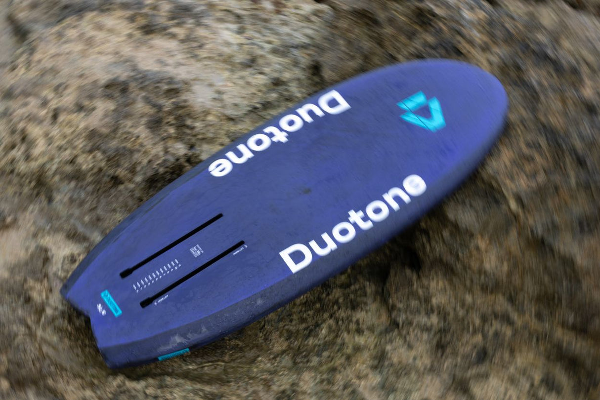 Duotone Crush SLS 2027 Kiteboard in Blau, Draufsicht auf Kiesuntergrund, mit Duotone-Logo und türkisen Akzenten