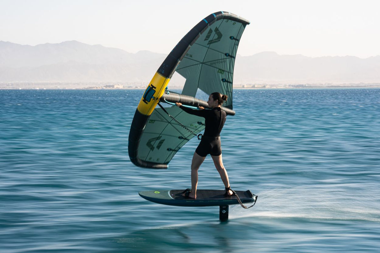 Duotone Skybrid SLS 2027 Kitesegel in Grün-Schwarz mit gelbem Gestänge, Athlet beim Kitesurfen auf dem Wasser in Seitenansicht