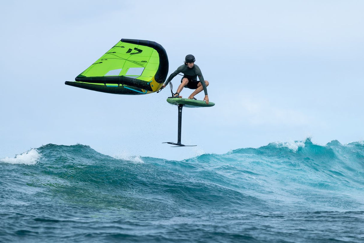 Duotone Trace SLS 2027 Kiteboard neongelb-schwarz, Athlet in Aktion über Wellen, Foil-Setup, Frontansicht