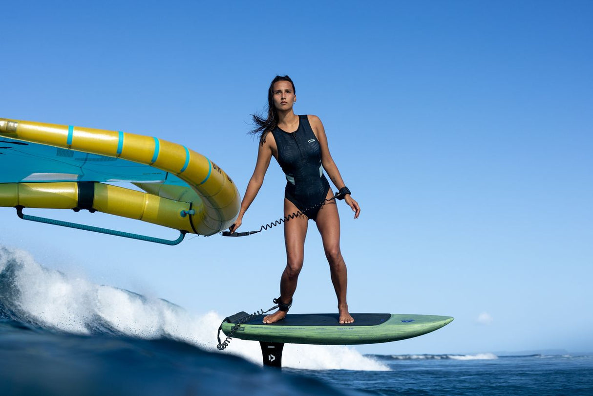 Duotone Trace SLS 2027 Kiteboard grün mit schwarzem Neoprenanzug, Frontalansicht auf dem Wasser mit Kite