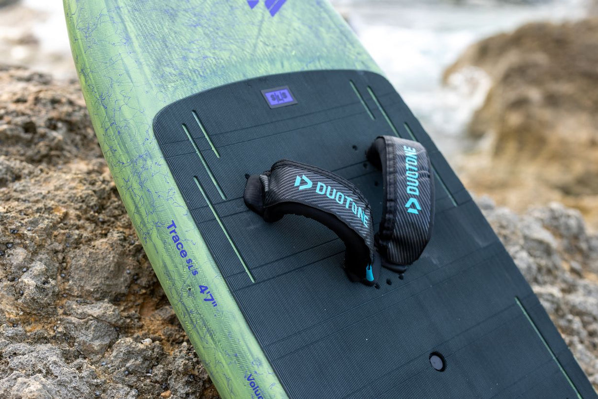 Duotone Trace SLS 2027 Kiteboard grün-blau mit schwarzem Footpad und Bindung, Draufsicht auf Stein