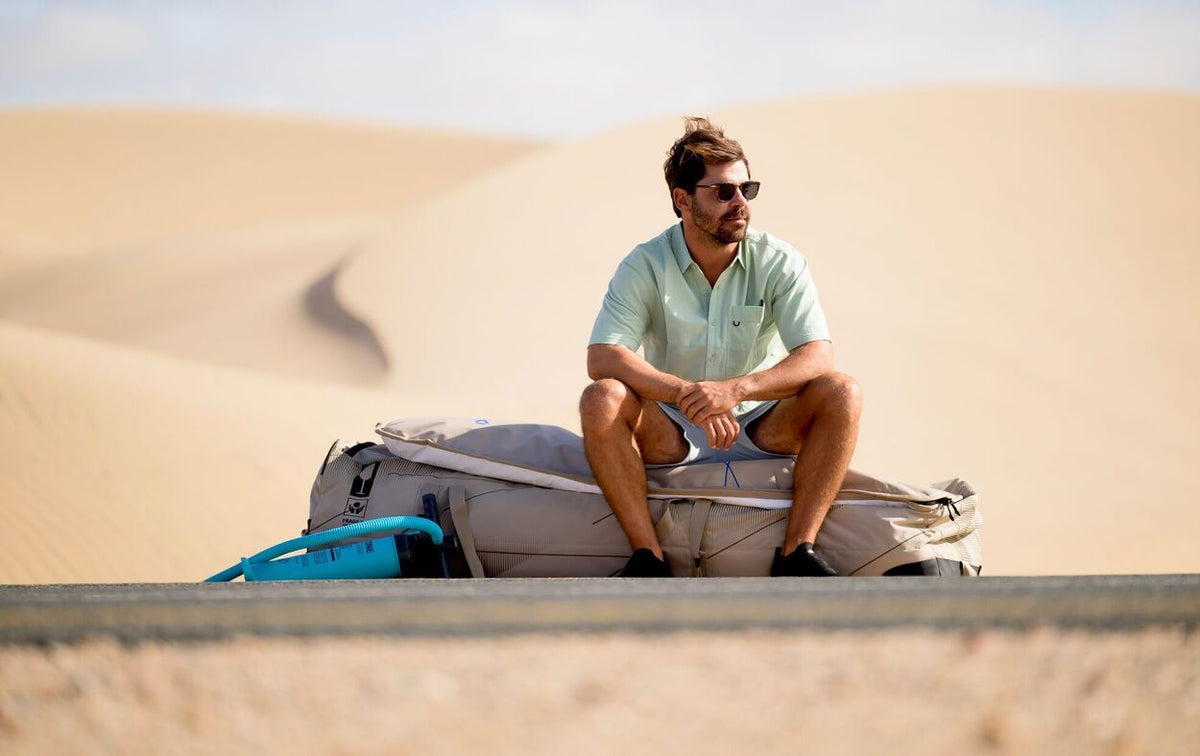 Duotone Boardbag Single Compact 2027 in Grau und Blau, Mann sitzt darauf in Wüstenlandschaft
