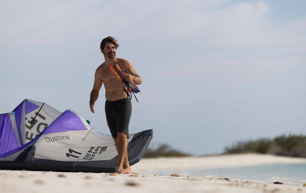 Duotone Trust Bar Quad Control 2027 Kiteboard in Weiß und Lila, am Strand von einem Sportler getragen