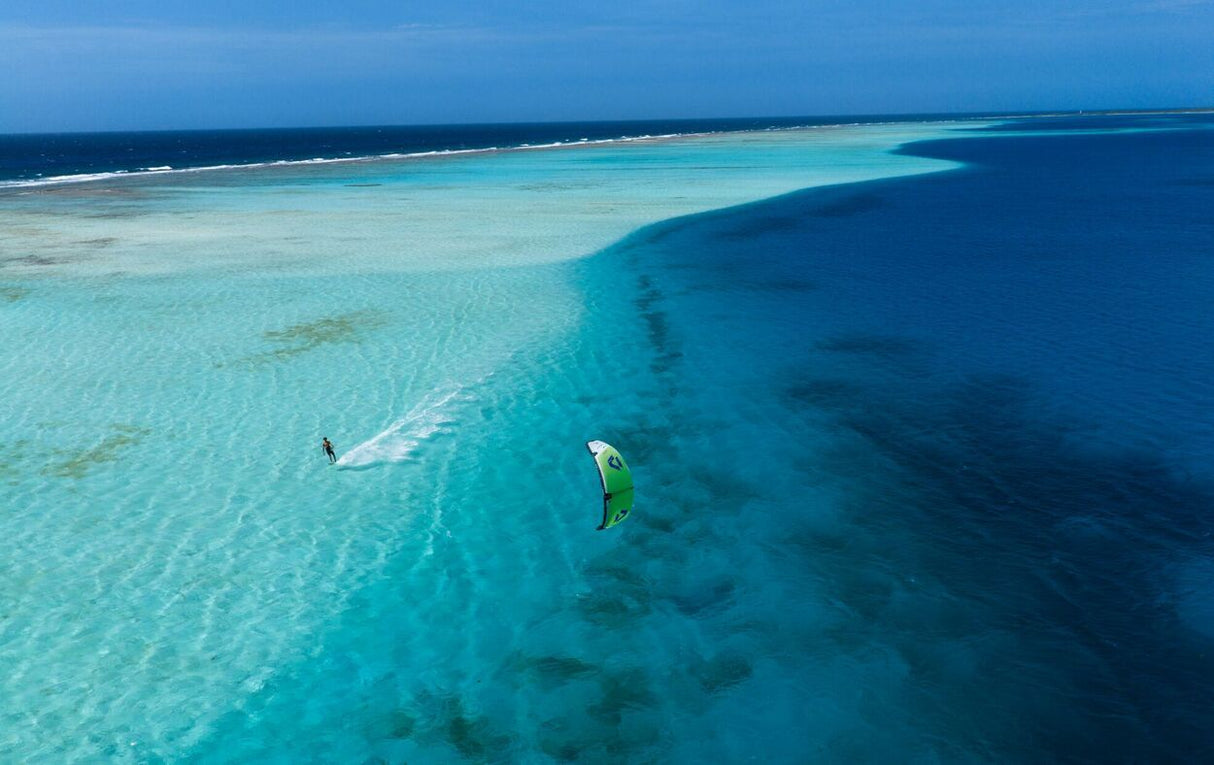 Duotone Blur SLS 2027 Kitesurfboard in Blau und Grün, Aerial-Perspektive über tropischem Wasser mit Kitesurfern