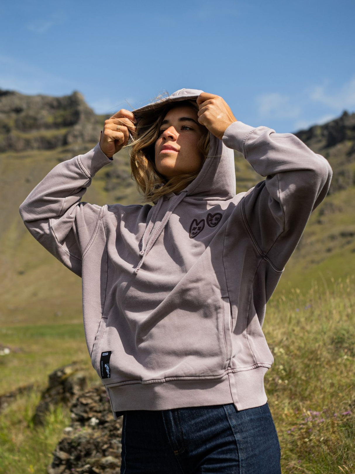 ION Hoody No Bad Days 2026 in Hellgrau, Kapuzenpullover mit Reißverschluss, getragen mit Kappe in grüner Berglandschaft