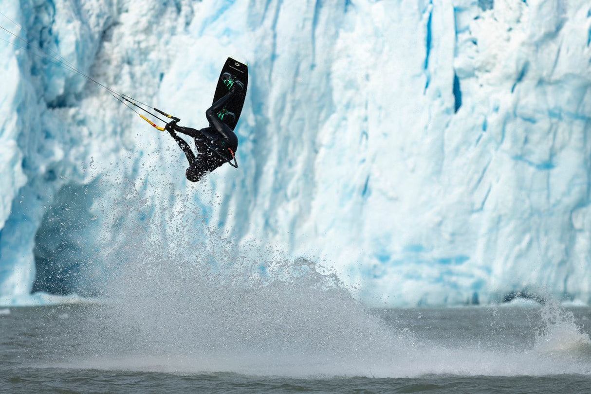 ION Claw Gloves 2026 schwarze Kiteboarding-Handschuhe, Athlet in Aktion über Wasser mit Eiswand im Hintergrund