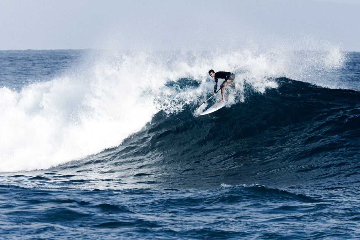 ION Wing SUP Board Leash Core Coiled Knee in Anwendung beim Wellenreiten, schwarze Spiralleine am Bein eines Surfers