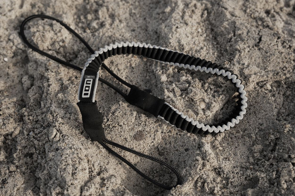ION Uphaul Line TEC 2026 schwarze Trapezleine mit weißem Elastikband und Handschlaufe auf Sand, Draufsicht