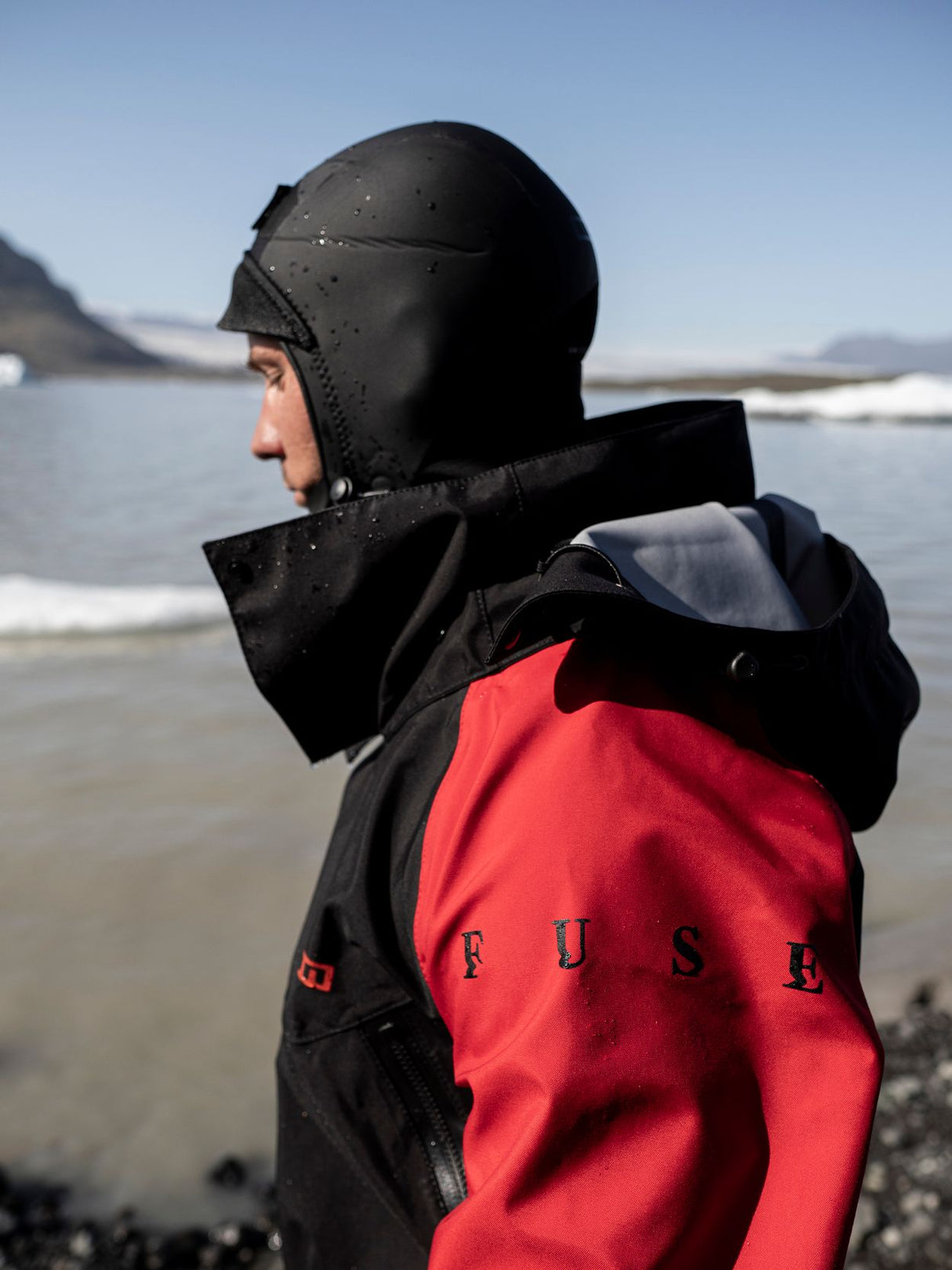 ION Fuse Lightweight Drysuit Back Zip 2026 in Rot-Schwarz, Rückenansicht am Strand getragen