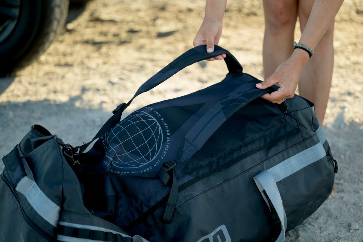 ION Suspect Duffel Bag 2024 in Schwarz mit Reflektorelementen, in Händen gehalten, Draufsicht