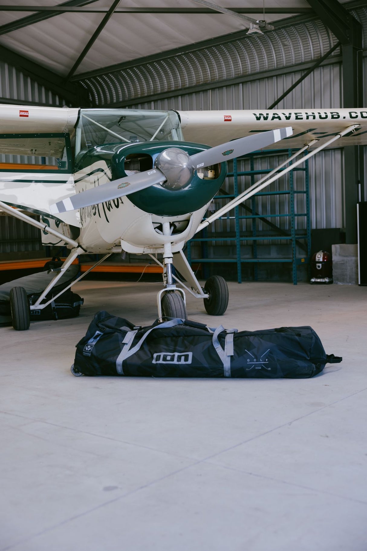ION Gearbag Tec Golf 2026 Tragetasche in Dunkelblau und Grau, entfaltet unter einem Flugzeug in Hangar