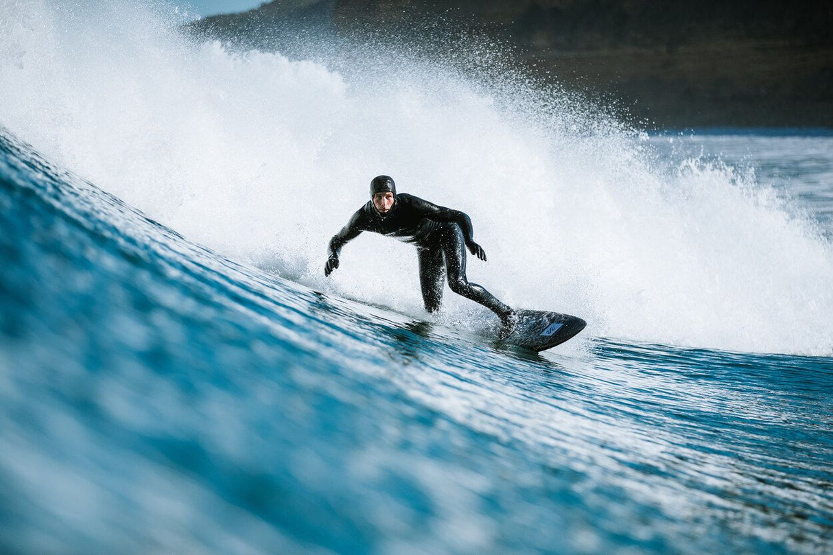 Surfer in schwarzem Neoprenanzug mit ION Ballistic Boots 6/5 Internal Split beim Wellenreiten, Frontalansicht