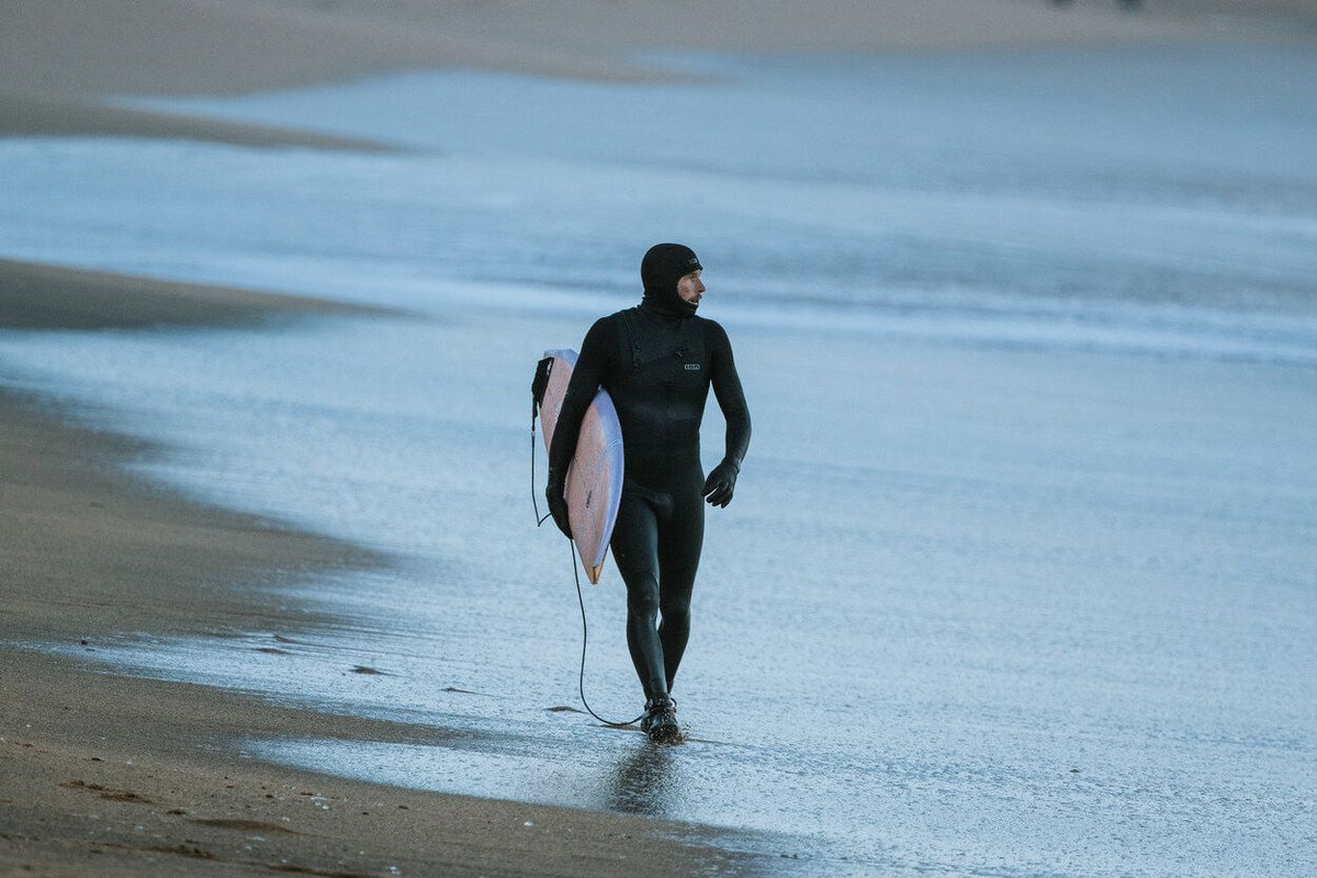 ION Ballistic Boots 6/5 Internal Split schwarz, Surfer trägt Neoprenanzug und Stiefel am Strand