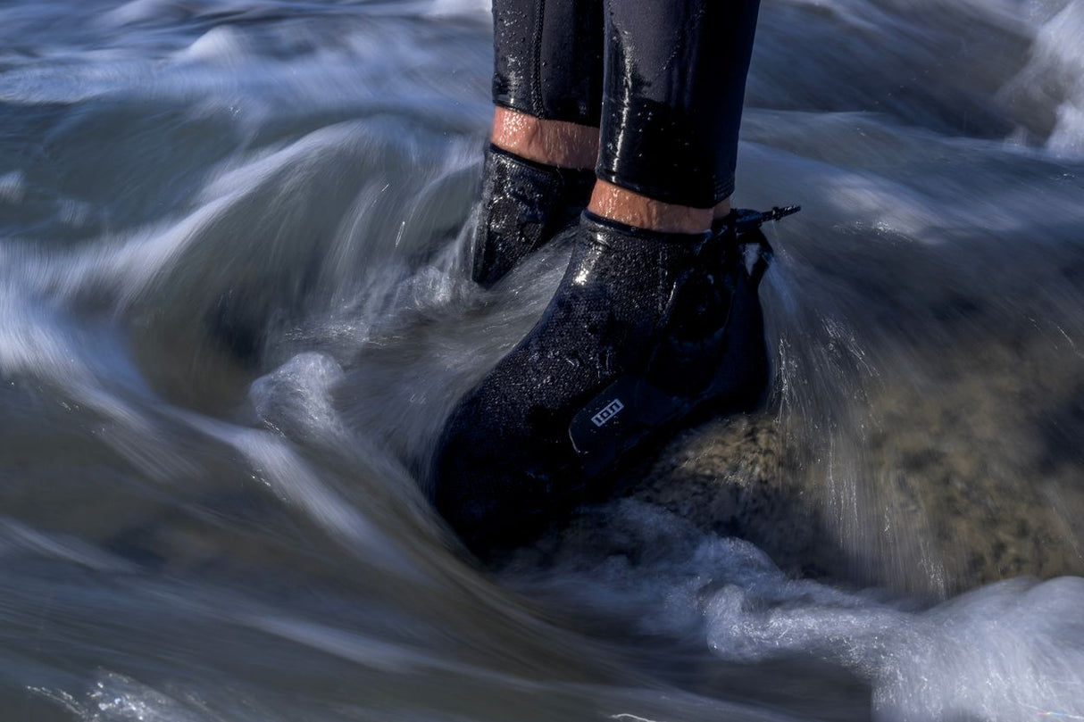 ION Ballistic Socks 6/5 schwarz mit kupferfarbenen Bändern, getragen im Wasser, Nahaufnahme der Füße