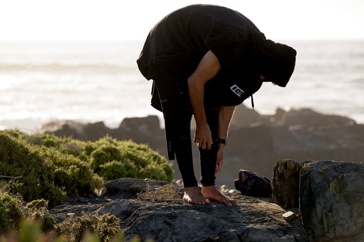 ION Poncho Core 2026 schwarz, Athlet beim Anziehen am Strand, Neopren-Umhang von vorne