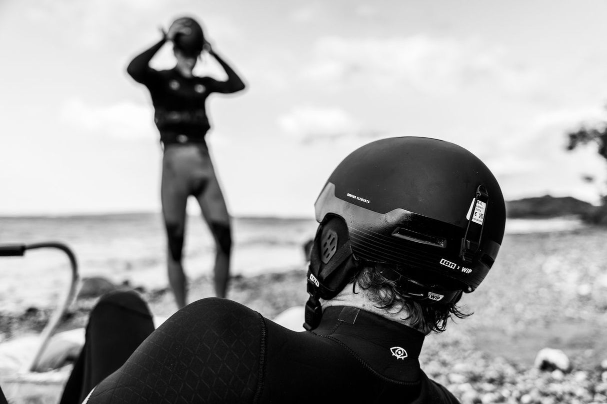 ION Mission 2026 Helm schwarz, Wassersportausrüstung mit Athlet am Strand, Vorderansicht