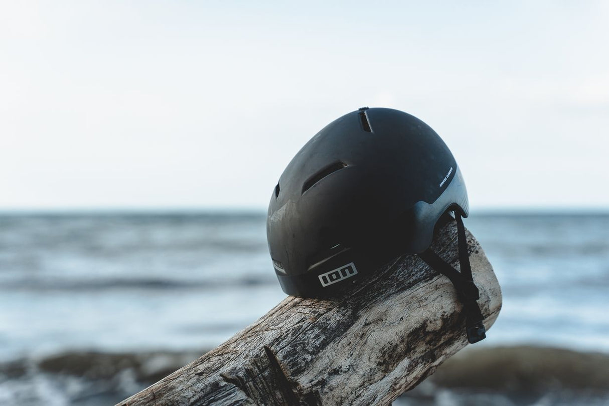 ION Mission 2026 Helm schwarz, Frontalansicht auf Holz am Strand mit Meereshintergrund